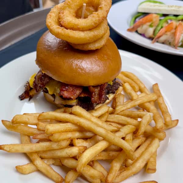 Bacon cheeseburger with onion rings and golden French fries at a casual American restaurant