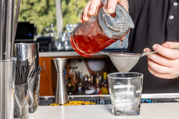 Bartender straining a handcrafted cocktail over a large ice cube at the restaurant bar.