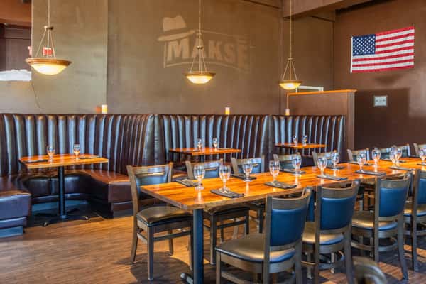 Modern Makse restaurant interior with leather booths, wooden dining tables, pendant lighting, and an American flag.