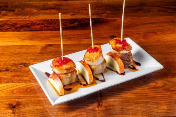 Seared scallop and pork belly bites with apple slices, red roe, and balsamic glaze served as a restaurant appetizer.