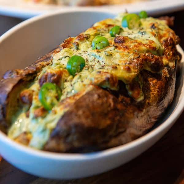 Loaded baked potato topped with melted cheese, jalapeños, and savory toppings at a casual American restaurant