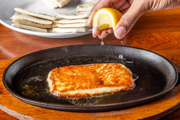 Grilled halloumi cheese sizzling in a cast iron skillet as fresh lemon juice is squeezed on top, served with warm pita bread.