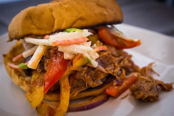 A hot sandwich with meat topped with red and yellow peppers and slaw