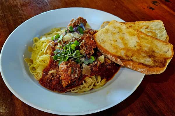 Spaghetti with marinara sauce and meatballs, topped with parmesan and microgreens, served with two slices of toasted garlic bread.