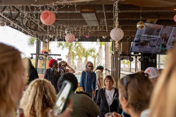 Live reggae performance at a festive beachside venue decorated with string lights and heart-themed lanterns, with a crowd watching.