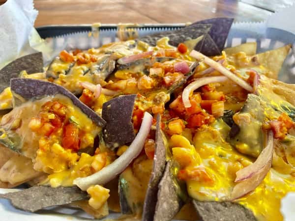 Colorful nachos topped with melted cheese, diced tomatoes, red onions, and jalapeños in a basket tray.