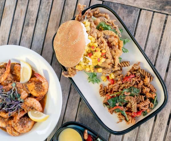 Fried soft-shell crab sandwich with mango salsa, served with a side of seasoned pasta salad and a lemon shrimp appetizer.