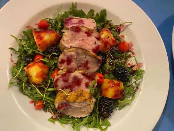 Sliced pork tenderloin with berry glaze over arugula, grilled pineapple, blackberries, cherry tomatoes, and blueberries.