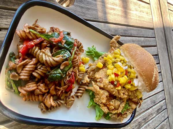 Soft shell crab sandwich topped with pineapple salsa, served with a side of rotini pasta salad with spinach and bell peppers.