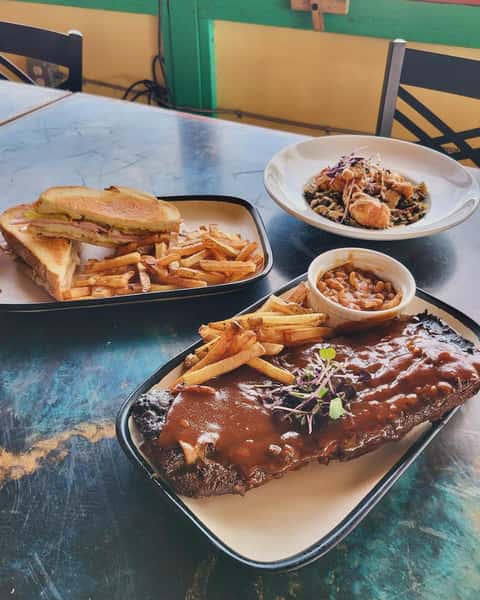 Barbecue ribs with fries and baked beans, a Cuban sandwich with fries, and a plate of fried catfish over greens in the background.