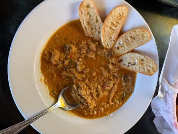Crab stew with mushrooms and peppers in a rich broth, served with toasted baguette slices on a white plate.
