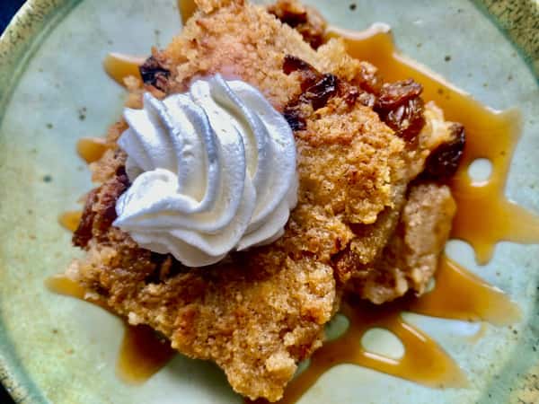 Bread pudding topped with whipped cream and drizzled caramel sauce on a green ceramic plate.