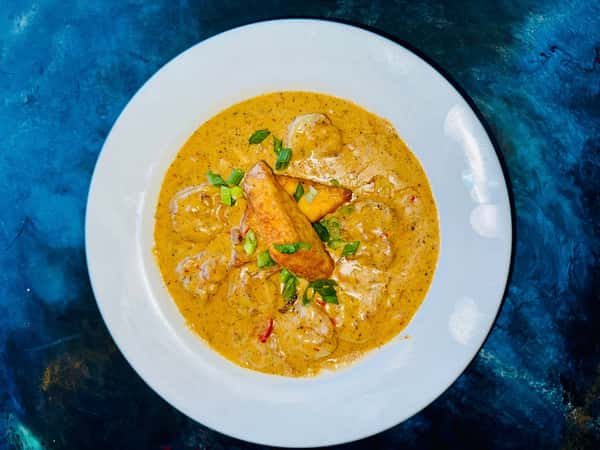 Shrimp in creamy Cajun sauce topped with fried plantains and garnished with chopped green onions on a white plate.