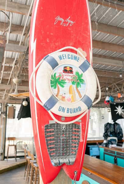 Red surfboard mounted indoors with a life ring reading "Welcome on board" and Red Bull Watermelon Margarita branding.