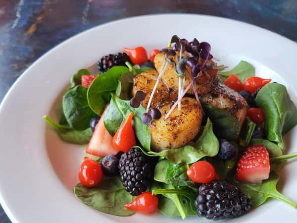 Seared scallops on a bed of spinach with blackberries, strawberries, blueberries, and cherry peppers, topped with microgreens.