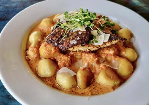 Blackened fish fillet served over gnocchi in a creamy tomato sauce, topped with shaved Parmesan and microgreens.