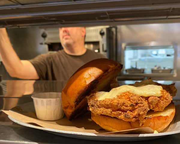 Chef Layne in kitchen with chicken sandwich on deck