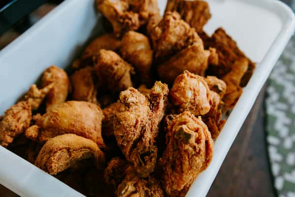 Large tray filled with crispy golden-brown fried chicken pieces, including drumsticks and thighs, ready to be served.