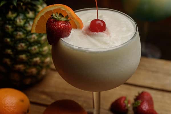 Beige colored drink in margarita glass with strawberry, lime, orange, and cherry