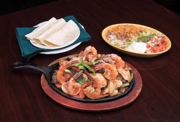 Variety of plates on table consisting of shrimp fajitas with egetables, rice, beans, and quesadillas