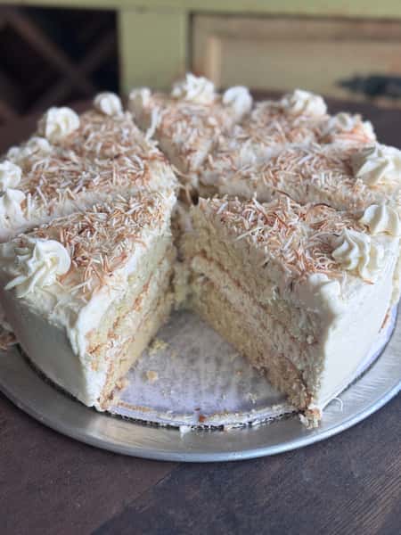 A white frosted cake topped with shredded toasted coconut, sliced and ready to serve.