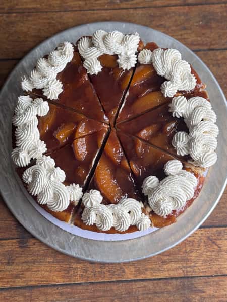 Peach upside-down cake topped with whipped cream and sliced into portions on a wooden table.