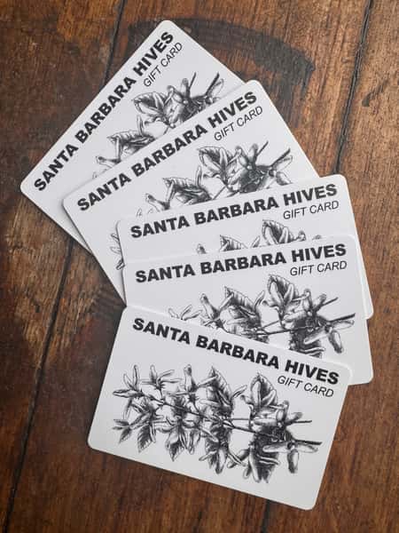 Santa Barbara Hives gift cards with a black and white botanical illustration, fanned out on a wooden surface.