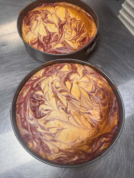 Two unbaked swirled cheesecakes in round pans, with marbled patterns of red and yellow batter.