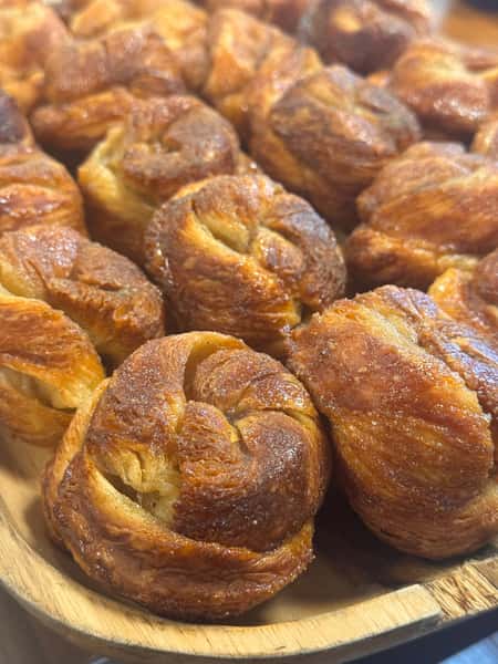 Golden, caramelized, and flaky pastry rolls displayed on a wooden tray.