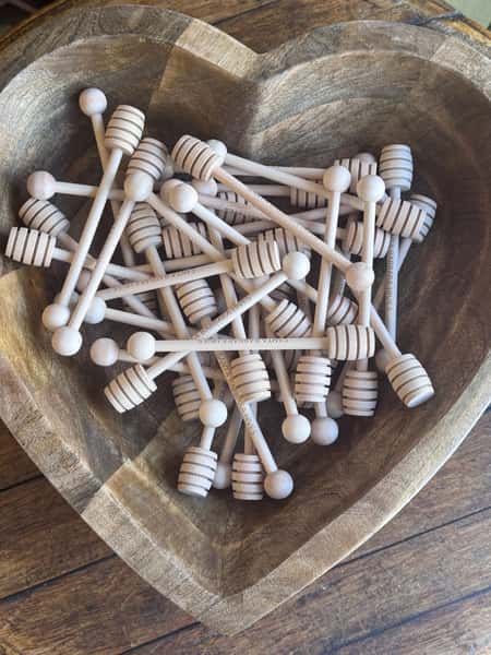 Wooden heart-shaped bowl filled with honey dippers engraved with 'Santa Barbara Hives'.