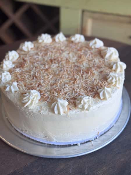 Whole coconut layer cake topped with shredded toasted coconut and whipped cream decorations