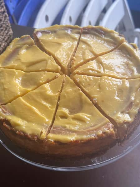 Sliced cheesecake with a yellow topping on a glass stand.