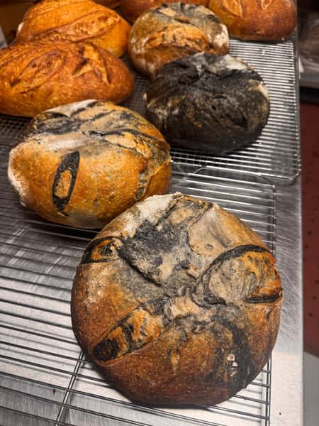Loaves of artisan bread with dark and golden crusts cooling on a wire rack.