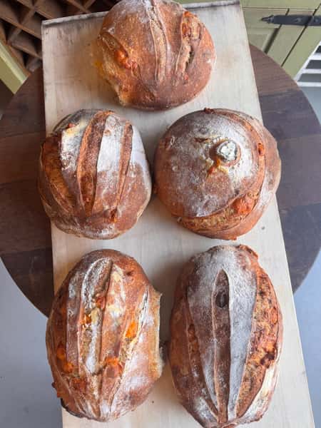 Five rustic loaves of bread with cracked crusts on a wooden board.