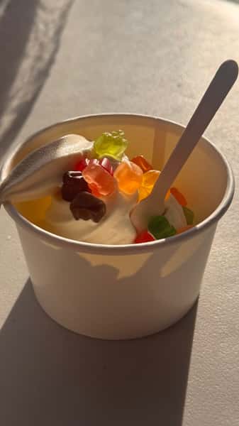Cup of soft serve ice cream topped with gummy bears, with spoon inserted.