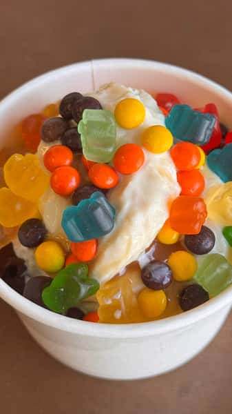 Ice cream topped with gummy bears and candy in a white cup.