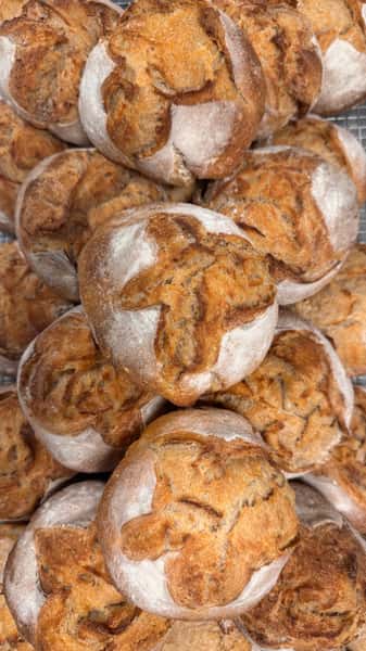 Pile of crusty round bread rolls with golden brown tops.