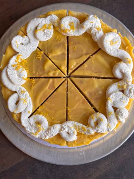 Lemon frosted cake with whipped cream topping, sliced into eight pieces.