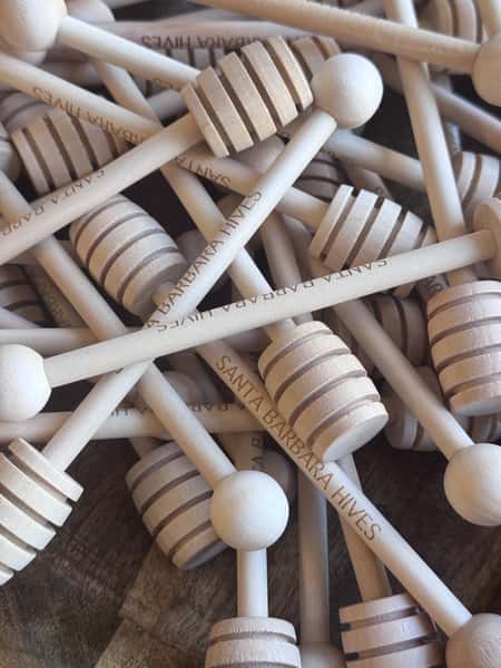 Pile of wooden honey dippers engraved with Santa Barbara Hives.