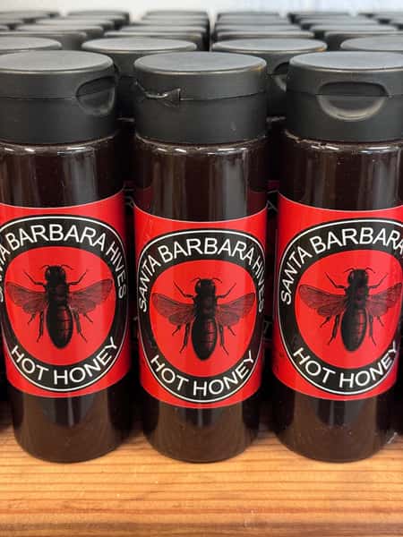 Santa Barbara Hives hot honey bottles with red labels lined up on a wooden shelf