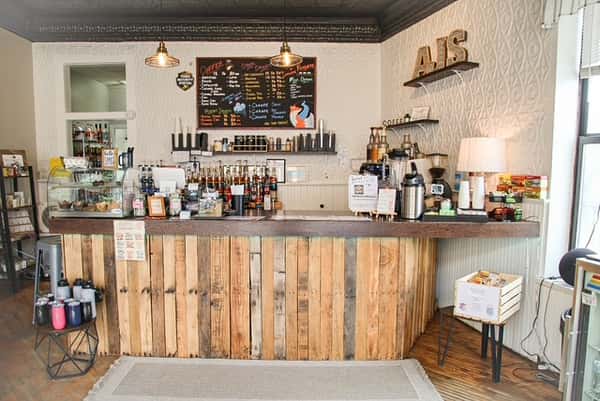 Warm interior of AJ's Riverside coffee shop featuring rustic wood counter, coffee bar, menu board, and bakery case.