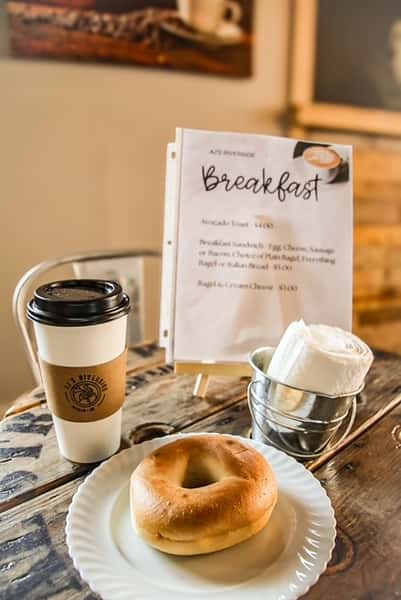 Warm breakfast scene with bagel, coffee, and menu at AJ's Riverside.