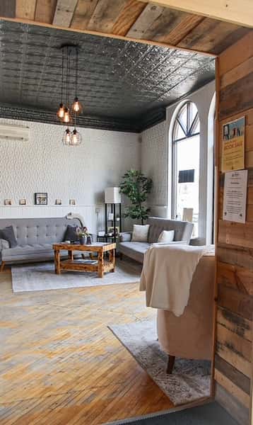 AJ's Riverside lounge featuring gray sofas, wood coffee table, textured wall, and dark tin ceiling.