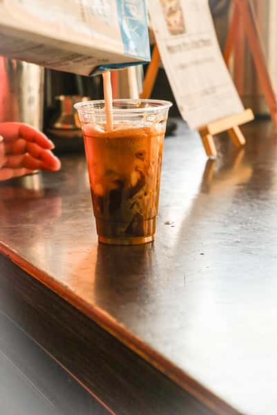 Milk pouring into a clear cup of layered iced coffee at AJ's Riverside.