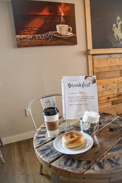 Bagel, coffee cup, and breakfast menu on a rustic table at AJ's Riverside.