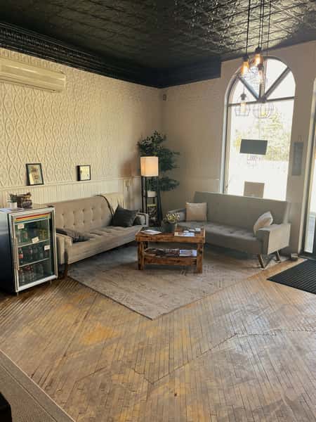 Cozy waiting area at AJ's Riverside featuring grey couches, patterned walls, wood block floor, and arched window.