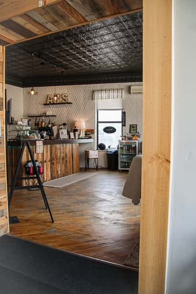 Warm interior view of AJ's Riverside featuring a rustic wood counter, wood floors, textured walls, and black ceiling tiles.