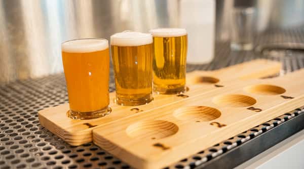 Three glasses of beer on a wooden flight board, with two filled with golden lager and one with a cloudy amber ale.