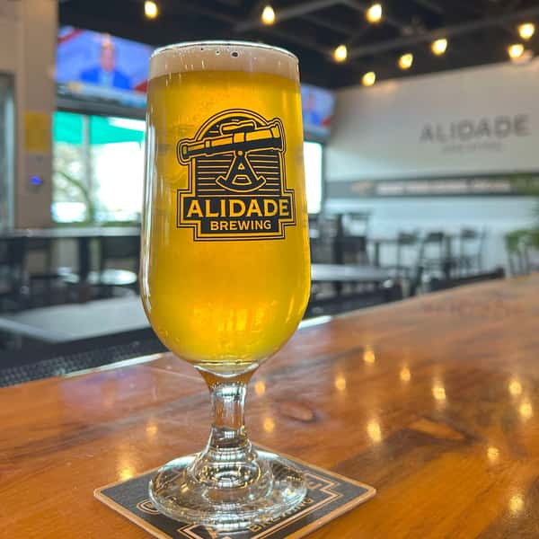 Freshly poured golden craft beer in an Alidade Brewing glass served inside the brewery taproom, featuring a crisp appearance, foamy head, and inviting pub atmosphere.