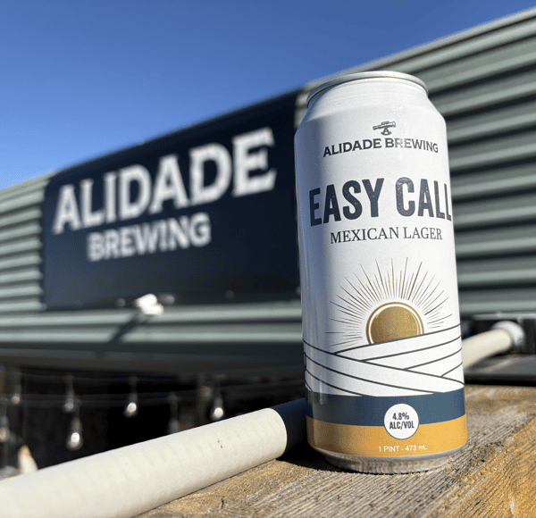 Can of Alidade Brewing Easy Call Mexican Lager displayed outside the brewery, showcasing a refreshing craft beer with the taproom in the background.